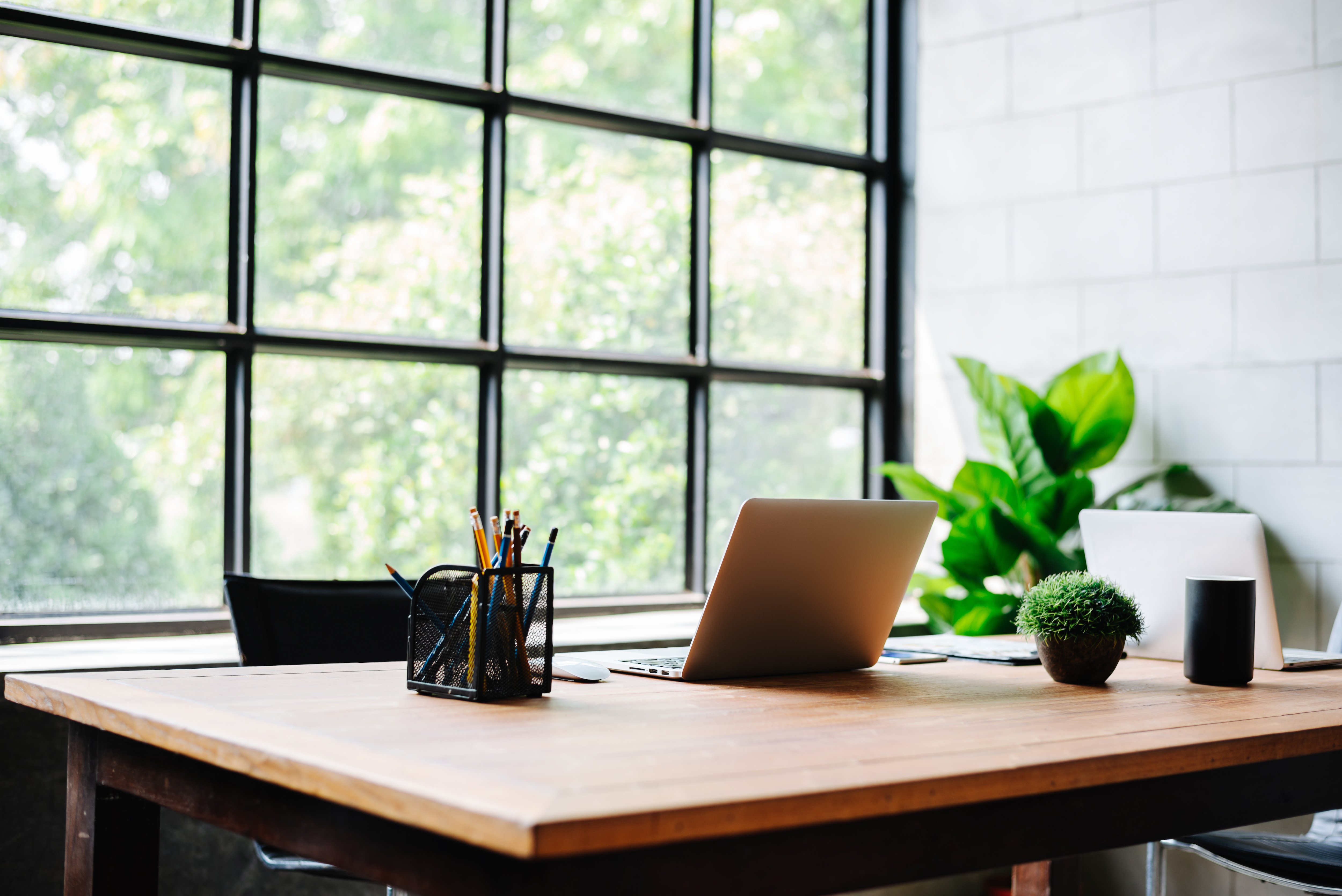 Home office with a light colored wooden desk with a large window behind it and a lot of natural light